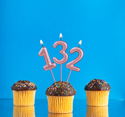 Three birthday cupcakes with number 132 candle - Blue background