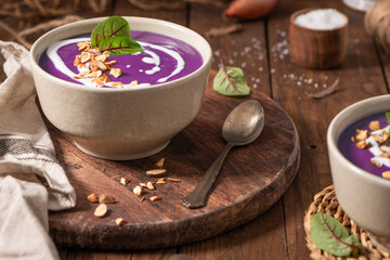 Healthy creamy red cabbage soup topped with herbs, a swirl of cream, toasted almonds, and fresh herbs, resting on a rustic wooden board.