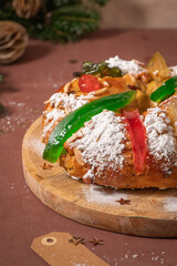 Colorful candied fruits and powdered sugar on a traditional Bolo Rei or Kings Cake, set on a wooden board amidst warm holiday decorations and lights. Is tradicional for Christmas in Portugal