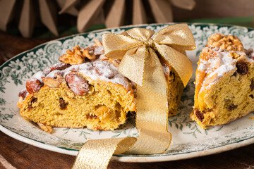 Bolo Rainha with a golden ribbon on a decorative plate, topped with nuts and powdered sugar, set on a wooden board with festive greenery around. Is a traditional dessert in Portugal during Christmas