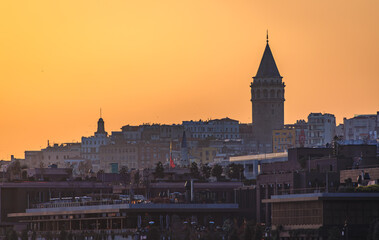 Naklejka premium Galata Tower silhouette stands against golden sunset sky, Istanbul cityscape layered with buildings and rooftops, urban skyline in Turkey at dusk