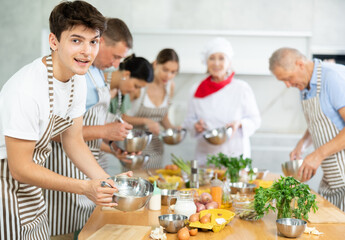 Young guy in apron learning to cook at cooking master class