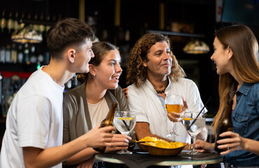 Group of friends standing at table in bar, drinking beer and having conversation.