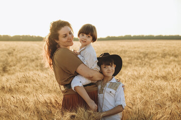 A young mother with two small sons on a walk in a wheat field in summer.