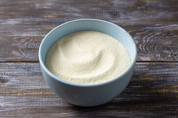 Light blue ceramic bowl filled with semolina sits on a textured wooden table