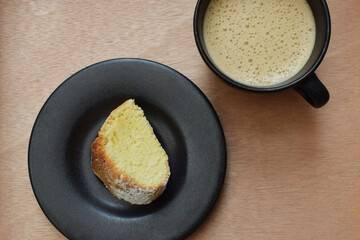 Taza de café capuchino y un trozo de pan dulce sobre una mesa de madera, plano horizontal.