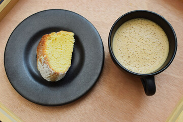 Taza de café capuchino y un trozo de pan dulce sobre una mesa de madera, toma cenital.