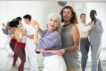 Positive elderly woman enjoying dancing in pair with expressive man during group training in dance...