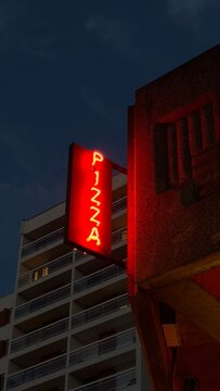 Bright neon pizza sign illuminated against an evening sky 