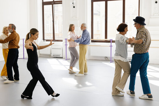 Old people dancing in pairs alongside professional dancer in ballroom