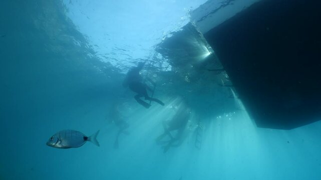 Scubadivers around the dive boat underwater with sun beams and rays