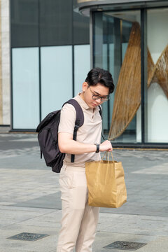 Man with shopping bag and backpack checking time on his watch