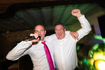 Two cheerful men singing karaoke and having fun at a party