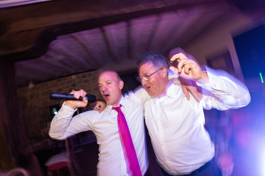 Two cheerful businessmen singing and dancing at night party