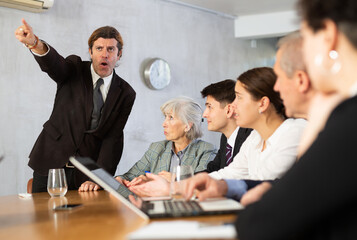 Angry male boss reprehending colleagues on meeting in modern office