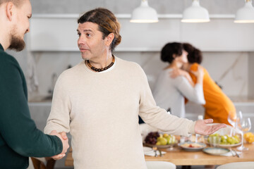 Fototapeta premium After chatting and gatherings, men shake hands, say goodbye, thank you for pleasant evening. Their girlfriends hug and kiss goodbye in background.