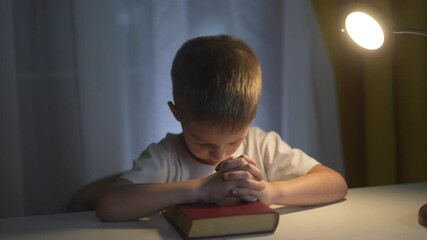 Lifestyle young boy is praying. A boy prays for a child religion. Religious book of prayer with hands on a table. A little boy is praying.