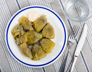 Plate is filled with baked vegetables topped with garlic sauce. Cooked artichoke cores with white hot sauce made from olive oil, garlic, egg yolks and lemon juice.