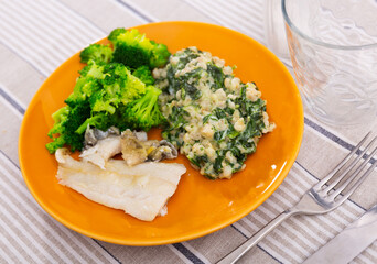 Cod with pearl barley porridge and boiled broccoli on a plate, side view. Low-calorie, nutritious lunch with fish and vegetables