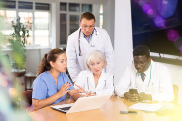 Obraz premium Medical workers sitting around the table watching something interesting at the display of notebook