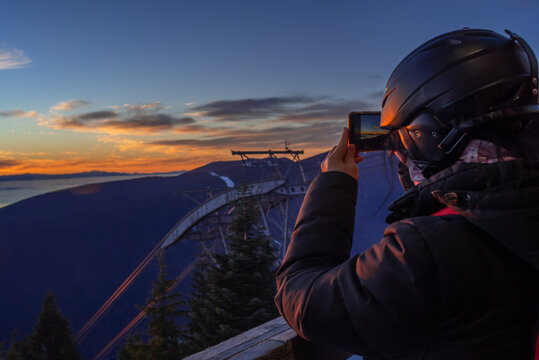 Anonymous person with ski helmet taking photo of sunset with phone