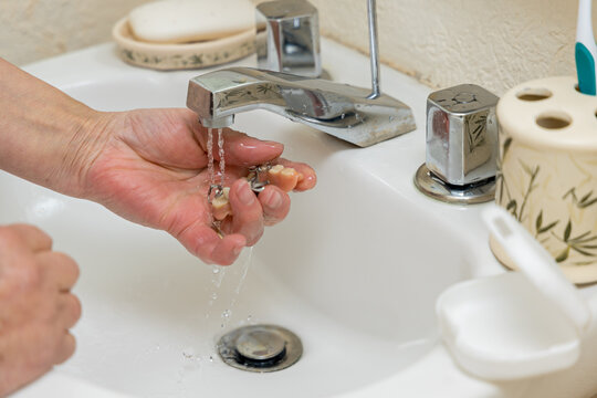 Hands of an unknown woman washing her dentures under tap water