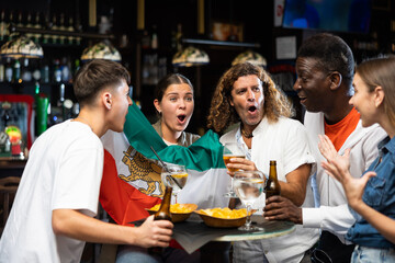 Group of Iran football team fans spending time in bar, drinking bear and having fun. People with state flag in pub.