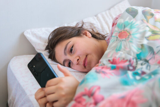 Young woman using smartphone in bed after waking up