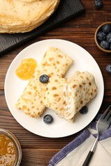 Delicious crepes with cottage cheese, jam and blueberries served on wooden table, flat lay