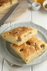 Pieces of delicious focaccia bread with olives, thyme, salt and knife on white wooden table, closeup