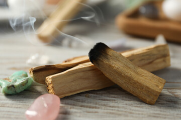 Smoldering palo santo stick and gemstones on wooden table, closeup