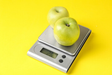 Electronic kitchen scale with apples on yellow background, closeup