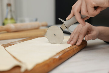 Woman cutting dough at light table, closeup. Making croissants