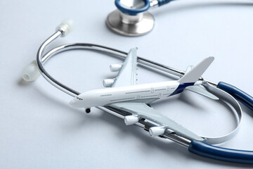 Medical tourism. Stethoscope and plane model on light grey background, closeup