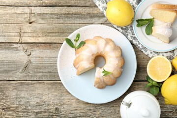 Delicious lemon cake with glaze, mint and citrus fruits on wooden table, flat lay. Space for text
