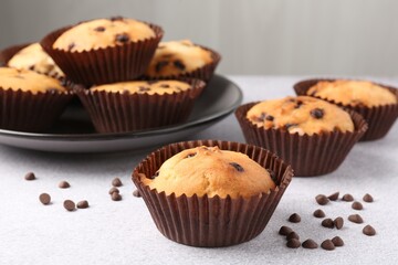 Delicious muffin with chocolate chips on light grey table, closeup