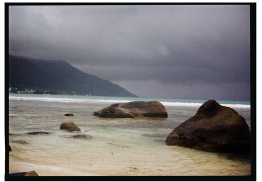 Dark clouds gather over a tranquil beach with rocky shoreline