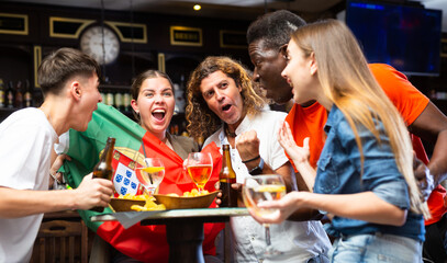 Happy international footbal fans waving the flag of Portugal while drinking beer and watching tournament in sport bar