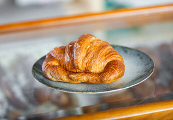 Fresh croissant with a golden crust on a plate in the bakery. Fragrant pastries for breakfast