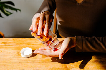 Sunlit detail of unnown lady taking multivitamin pills from a bottle