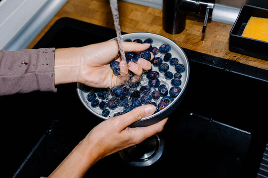 Close-up direct flash lit of unknown lady's hands washing blueberries
