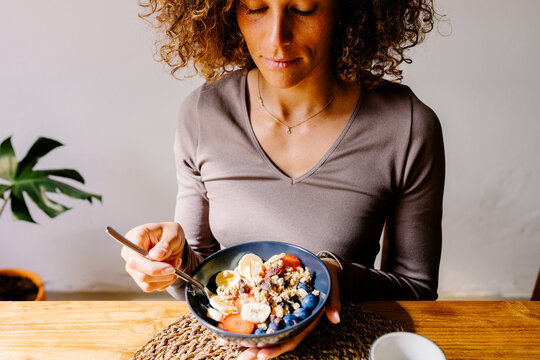 Latin woman holding a bowl of fruit and granola on a wooden table