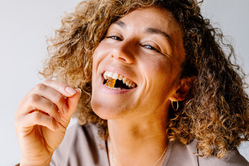 Brazilian woman smiling at camera while taking vitamin gummies