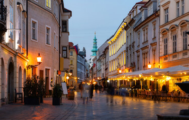 Rare passers-by walk along houses on Venturska Street in Bratislava. Evening twilight, cobblestone pavement on Ventura Street, evening time in old town.