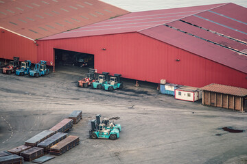 Forklifts parked near large red warehouse and metal sheets