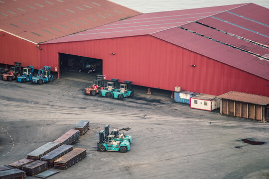 Forklifts parked near large red warehouse and metal sheets