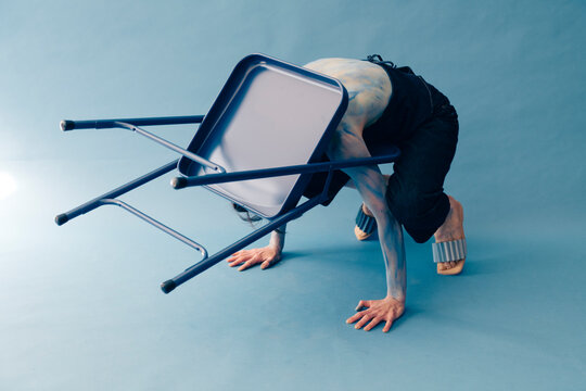 Individual Balancing Under a Blue Chair on an Artistic Pastel Ba