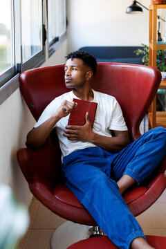 Pensive man in modern armchair writing journal at home. Hygge
