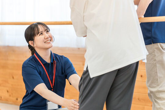 手すりを使い歩行訓練するシニア女性と介助する作業療法士,理学療法士の男女スタッフ
