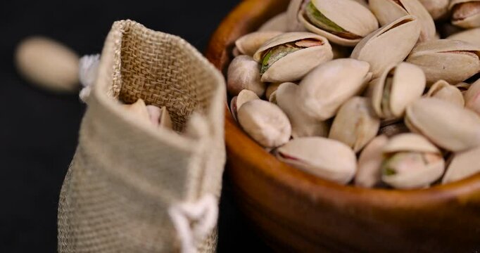 shelled pistachio nuts with added salt in a wooden bowl and a linen bag, unpeeled pistachio nuts with cracked shells, poured into a wooden bowl and a coarse bag